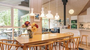 Une cuisine moderne avec des meubles blancs, une table à manger en bois et des luminaires suspendus.