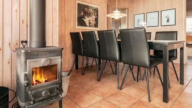 Un intérieur en bois agrémenté d’un poêle à bois, d’un coin repas avec des chaises et de tableaux encadrés accrochés au mur.