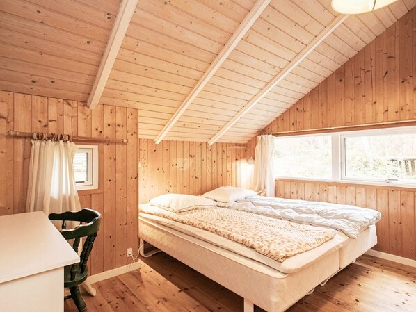 A wooden cabin bedroom with a bed, a chair, and a window.
