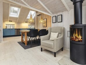 A cozy living room with a fireplace, a dining area with a table and chairs, and a kitchen with blue cabinets and wooden ceiling beams.