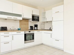 Una cocina moderna con armarios blancos, horno empotrado, microondas y cafetera.