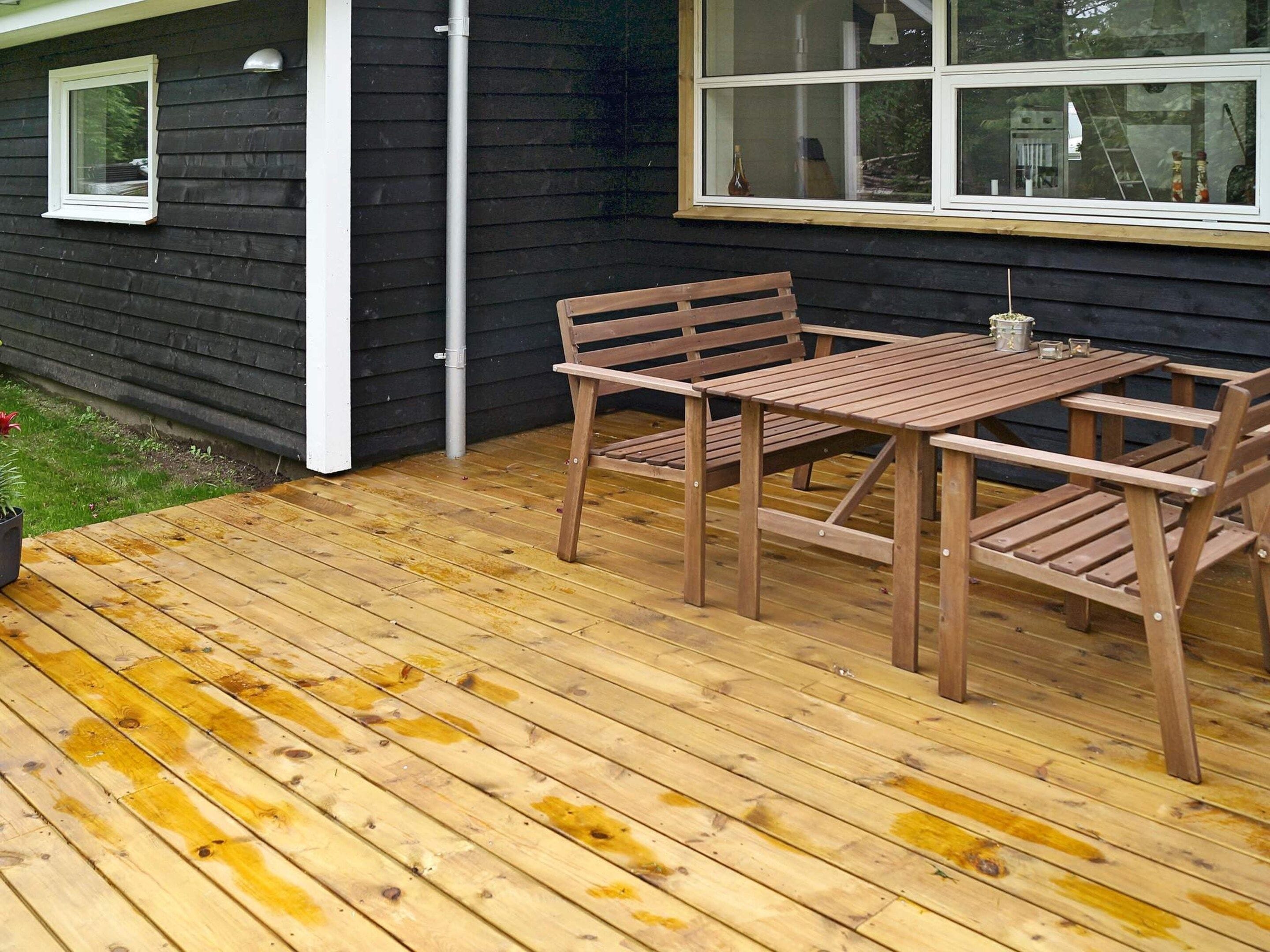 Een houten terras met een tafel, stoelen, een raam en een deur.