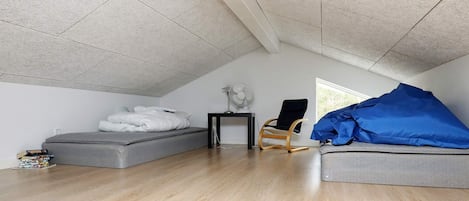 A room with a sloped ceiling, a bed, a chair, and a table with a lamp.