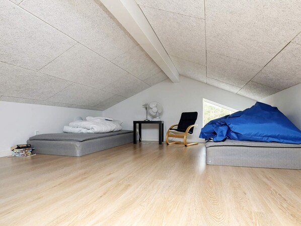 A room with a sloped ceiling, a bed, a chair, and a table with a lamp.