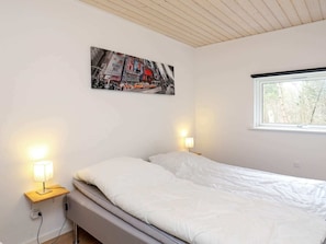 A bedroom with a bed, a nightstand with a lamp, a window, and a poster on the wall.