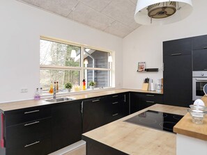 Una cocina moderna con armarios negros, encimera de madera, horno empotrado y ventana que proporciona luz natural.