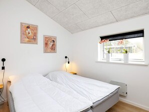 Un dormitorio con cama, dos lámparas de pared, una ventana con plantas en macetas y un radiador.