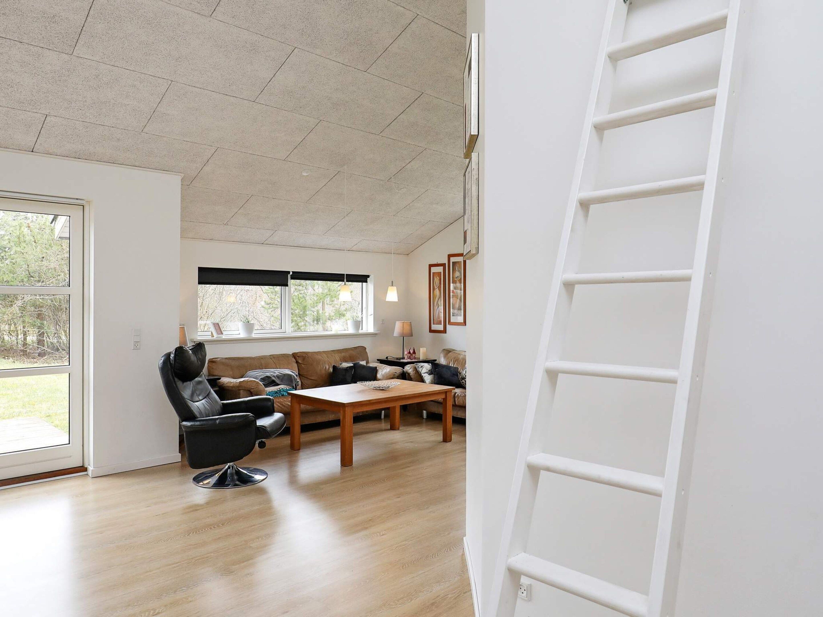 Amplia sala de estar con piso de madera, un sofá de cuero, una mesa de comedor y una escalera contra la pared.