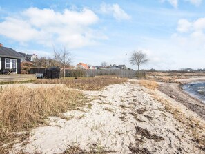 A sandy beach with a wooden fence, a house in the background, and a clear sky. - 4 Star Holiday Home in Bjert (Bjert)