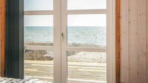 Una habitación con un amplio ventanal que da a una terraza de madera con vistas a la playa.
