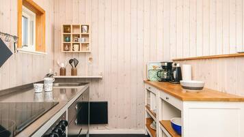 A compact kitchen with wooden walls, a built-in stove, and a coffee maker.