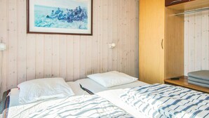 Un dormitorio con dos camas, un armario de madera, un cuadro enmarcado en la pared y una mesita de noche con una lámpara.