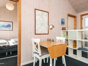 A room with a wooden floor, a dining table with chairs, a map on the wall, a bookshelf, and a bed with a suitcase. - 4 Star Holiday Home in Bjert (Bjert)