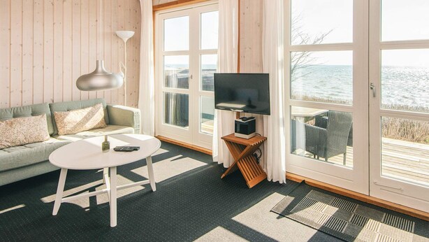 Una habitación acogedora con sofá, una mesa redonda, televisión y ventanas amplias con vistas al mar.