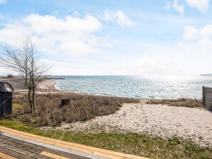 A beach view with a wooden deck, sandy beach, and a fence.