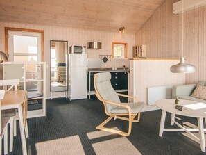 A compact kitchen with a refrigerator, microwave, and stove, a dining area with a table and chairs, and a seating area with a sofa and armchair.