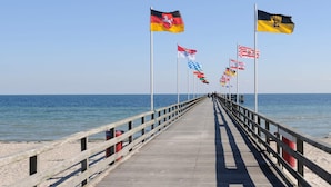 A wooden pier extending into the sea with multiple flags on poles. - Holiday Home in GroÃŸenbrode (Grossenbrode)