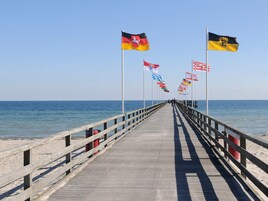A wooden pier extending into the sea with multiple flags on poles.
