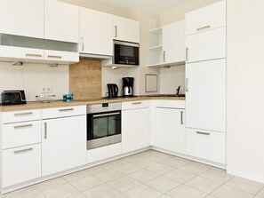A modern kitchen with white cabinetry, a built-in oven, a microwave, and a coffee maker.