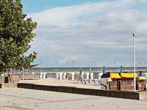A beachside promenade with rows of beach chairs and umbrellas, a concrete walkway, and a view of the sea.
