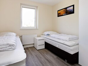 A bedroom with two beds, a window, a radiator, and a small bedside table.