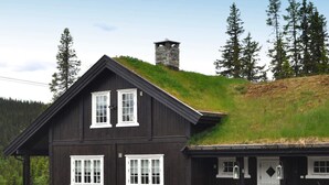 A two-story wooden house with white-framed windows, a stone chimney, and a grassy roof. - Holiday Home in FÃ¥vang (Ringebu)