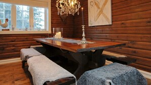 A cozy cabin interior with a wooden dining table, bench seating, a chandelier, and a window with a rooster decoration. - Holiday Home in FÃ¥vang (Ringebu)