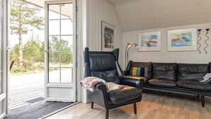 Ett rum med en svart läderfåtölj, en svart lädersoffa och ett trägolv. På väggen hänger tre inramade konstverk, och det finns en dörr som leder ut.