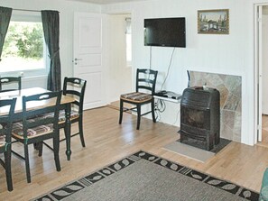 A room with a dining table, chairs, a flat-screen TV mounted on the wall, a fireplace, and a patterned rug. - Holiday Home in Vevang (Hustadvika)
