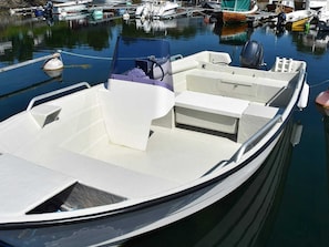 Um pequeno barco a motor branco atracado em um porto, com cabine e área de estar.