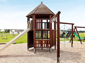 A playground with a wooden playhouse, a slide, and a climbing structure.