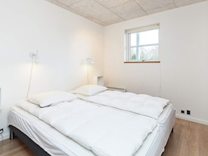 A bedroom with a bed, two bedside lamps, a window, and a wall-mounted heater.
