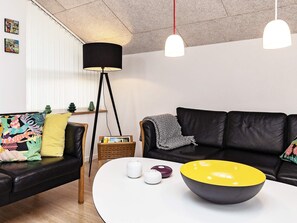 A modern living room with a black leather sofa, a round coffee table with decorative items, a floor lamp, and a wall-mounted light fixture. - 5 Star Holiday Home in Brovst (Brovst)