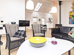A modern living room with a sofa, two armchairs, a coffee table, and a TV.