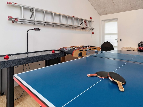 A room with a ping pong table, a foosball table, and a ladder against the wall.