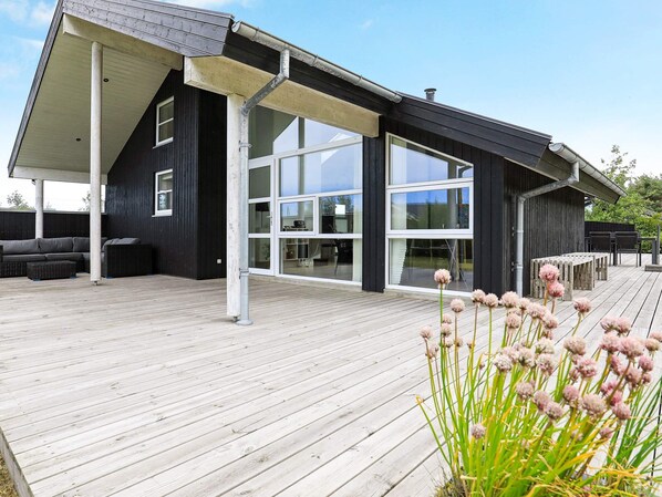 Uma casa moderna com varanda coberta, janelas amplas e deck de madeira.