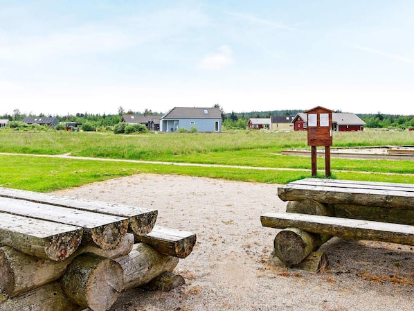 A gravel area with wooden benches and a wooden structure, likely a lookout or shelter, in a rural setting with houses in the background.