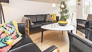 A modern living room with a black leather sofa, a round white table, and a potted plant. - 5 Star Holiday Home in Brovst (Brovst)