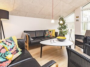 A modern living room with a black leather sofa, a round white table, and a potted plant.