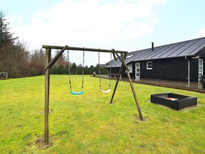 A wooden swing set in a grassy yard with a house in the background.