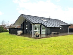 A modern house with a large glass door entrance, a covered patio, and a metal roof.