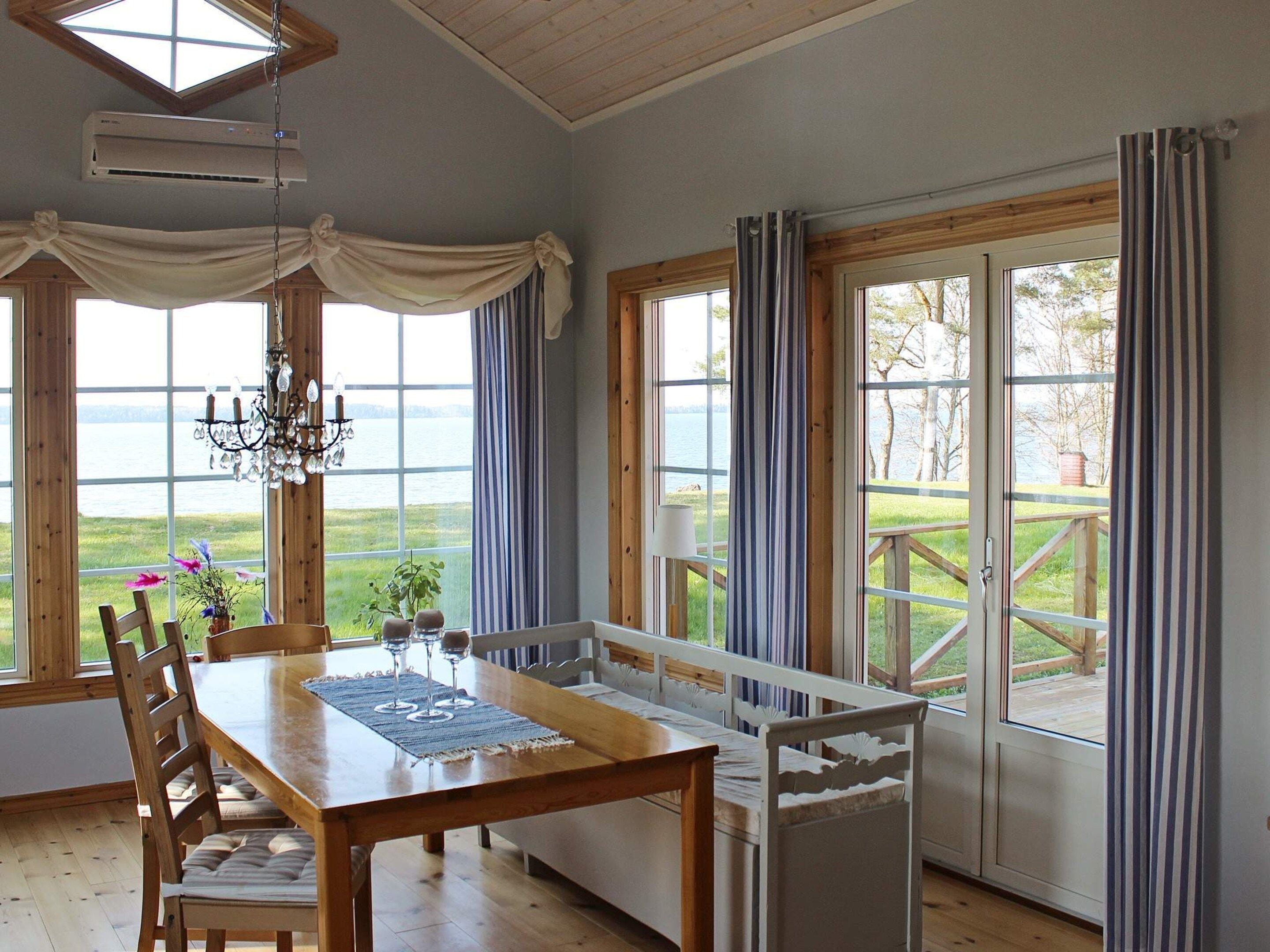 A dining area with a wooden table and chairs, large windows with curtains, and a view of a lake.
