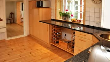 Una cocina con armarios de madera, una estantería para vinos, un microondas y un reloj en la pared.