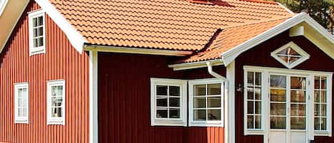 A red wooden house with a sloped roof and multiple windows.
