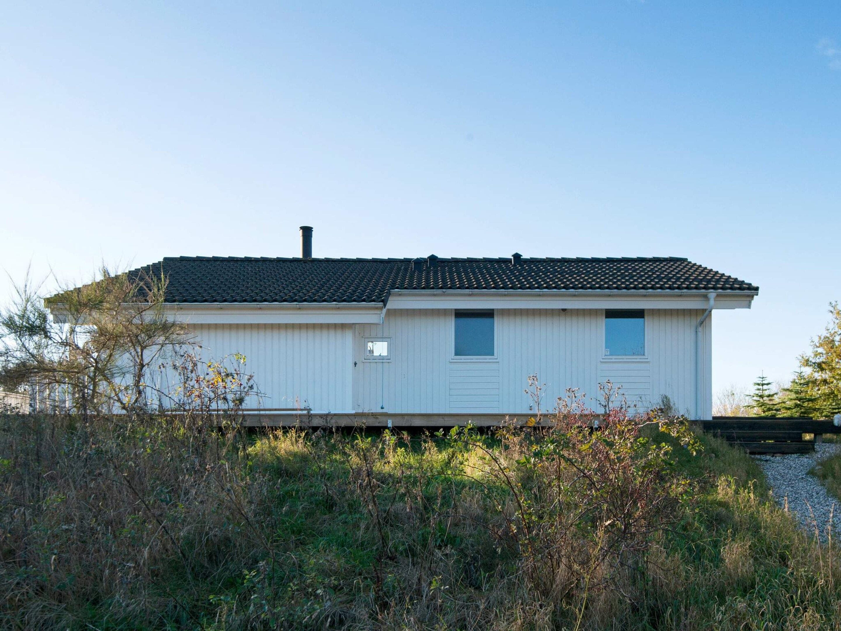 A single-story white building with a dark roof, surrounded by overgrown vegetation.
