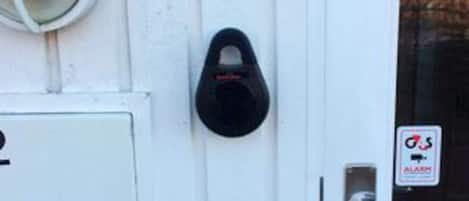 A door with a black security device, a white door frame, and a small sign with a red and white logo.