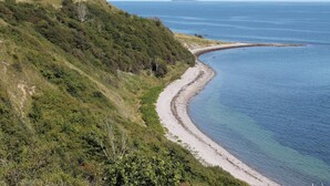 A coastal landscape with a curving beach, grassy hills, and a distant island.