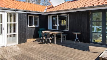 Una terraza de madera con una mesa, sillas, un ventanal corredero y una ventana.
