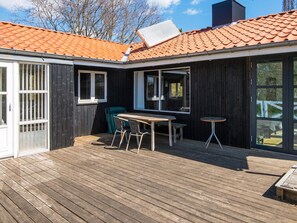 Une terrasse en bois avec une table et des chaises, une porte-fenêtre coulissante et une fenêtre.