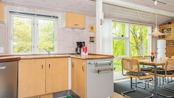 Una cocina con armarios de madera, cafetera integrada y un comedor con mesa y sillas.